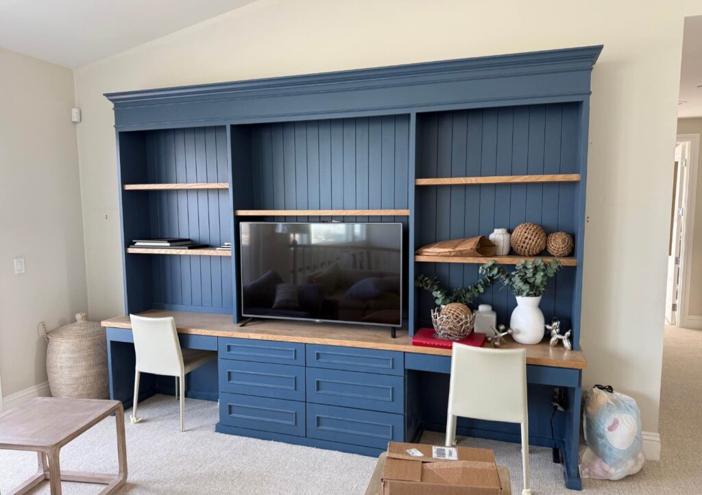 Custom blue home office built-in cabinets with TV, shelves, and desk in Houston home