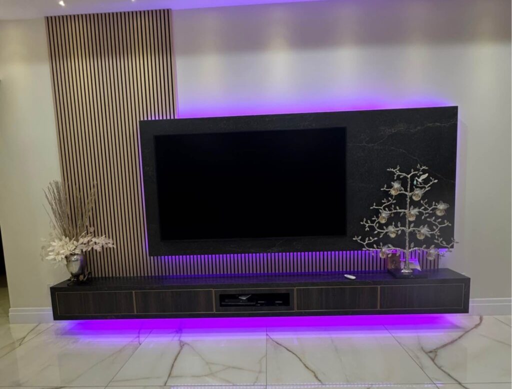 Custom media wall with wood slat accent panel, TV, floating cabinet, and purple LED lighting in Houston home